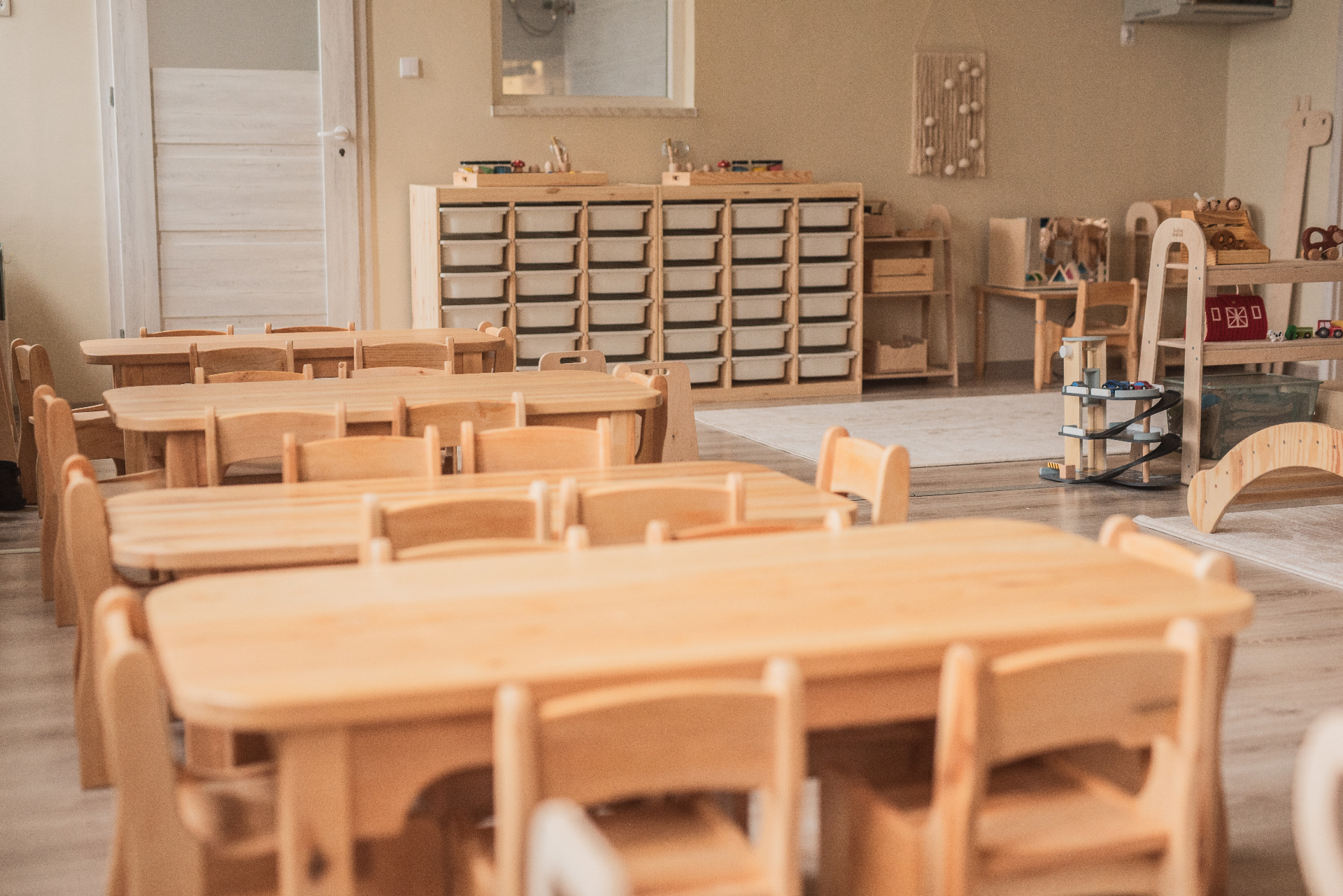 Sala przedszkolna z drewnianymi stolikami i krzesełkami
